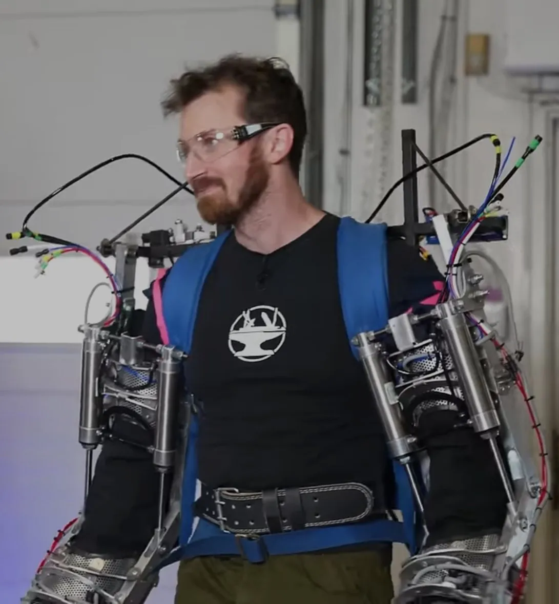 An engineer wearing the power-armor exoskeleton arms, with pneumatic cylinders and hoses running along each arm.