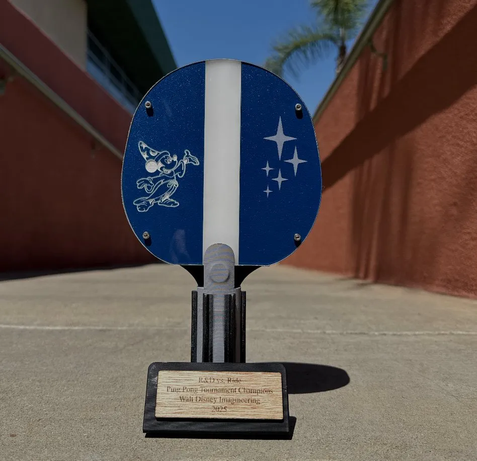 A paddle-shaped trophy with an engraved Sorcerer Mickey and stars, standing on a wooden plaque base.