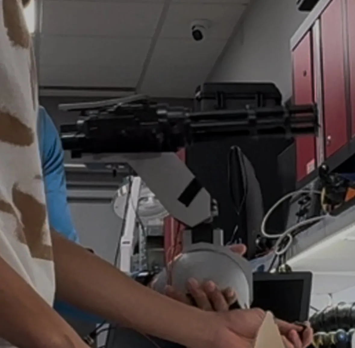 A shoulder-mounted rotary-barrel turret on a pan-tilt mount, being adjusted by hand.