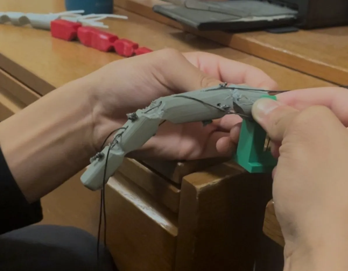 Hands holding a gray 3D-printed robotic finger strung with tendon lines.