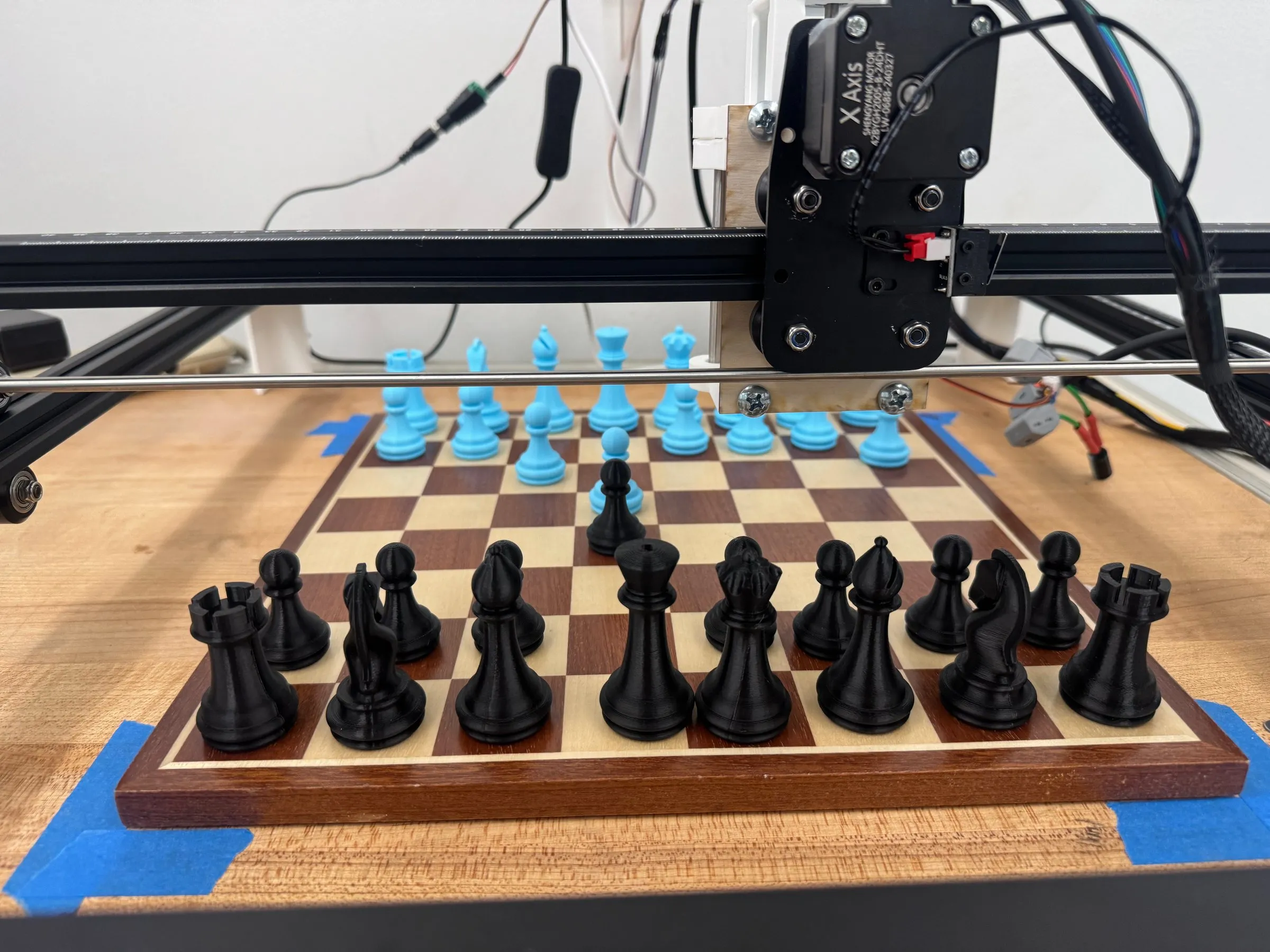 Front view of the gantry carriage above the chessboard, with black pieces in the foreground.