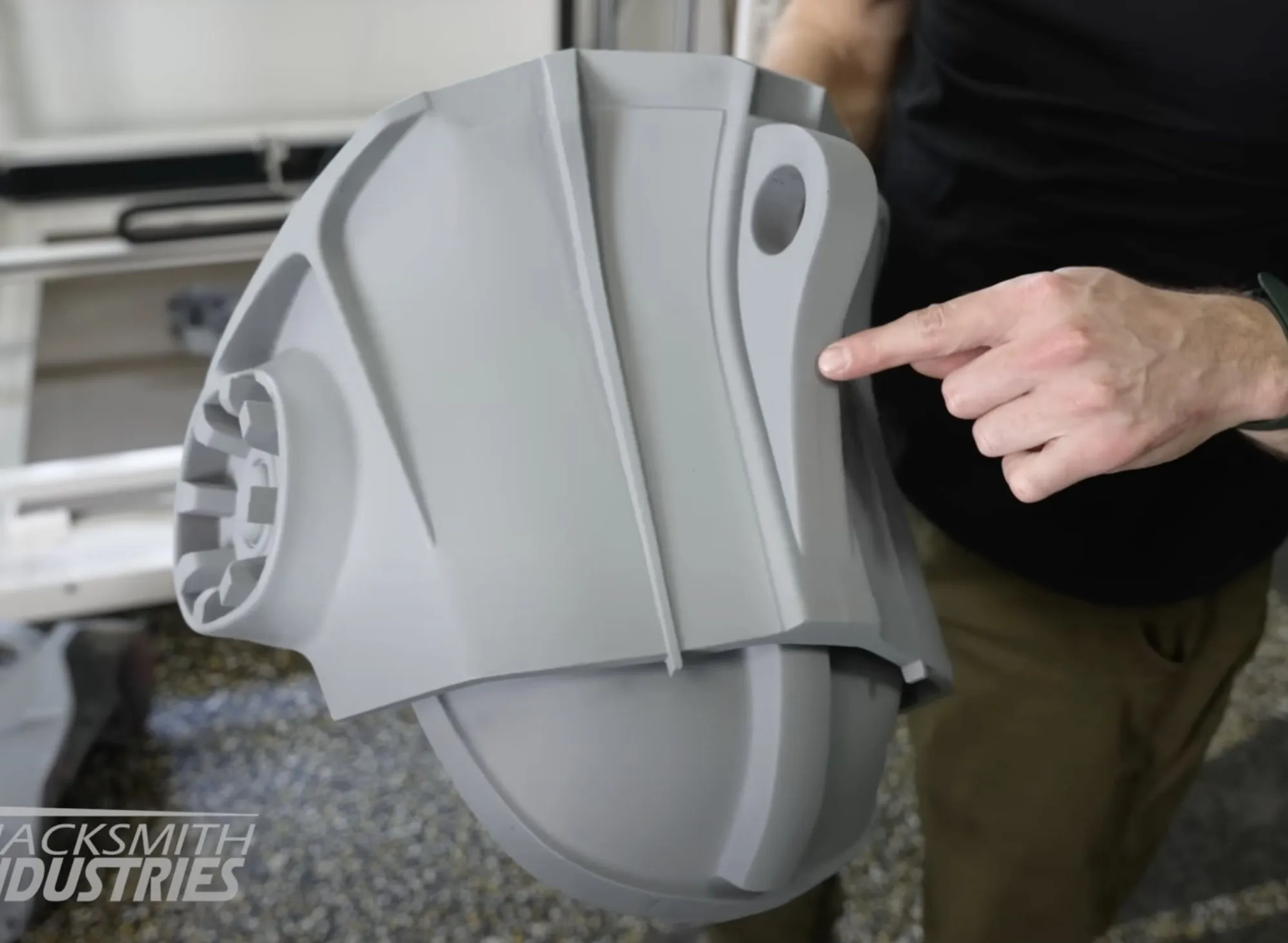 A large gray 3D-printed armor piece being inspected by hand.