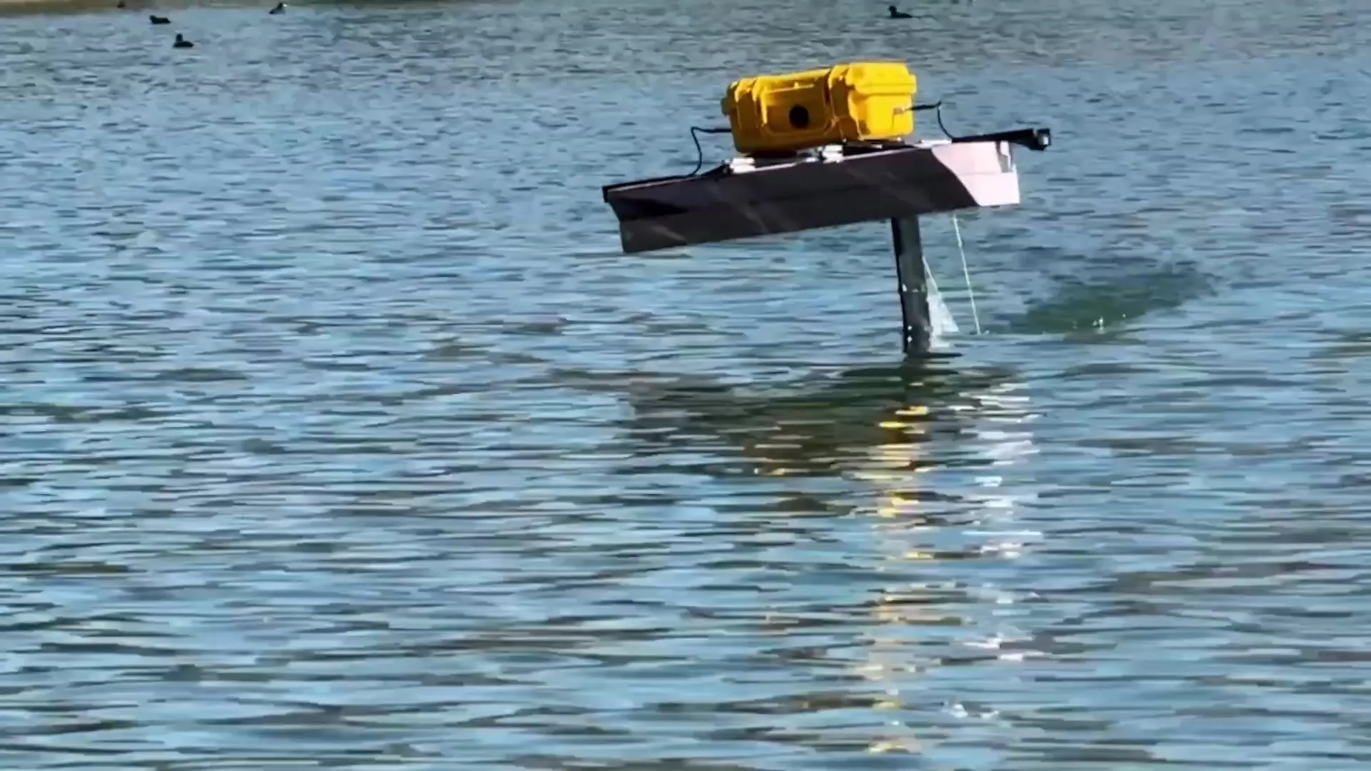 The early test platform, a pink foam deck with a yellow electronics case, riding on the hydrofoil.